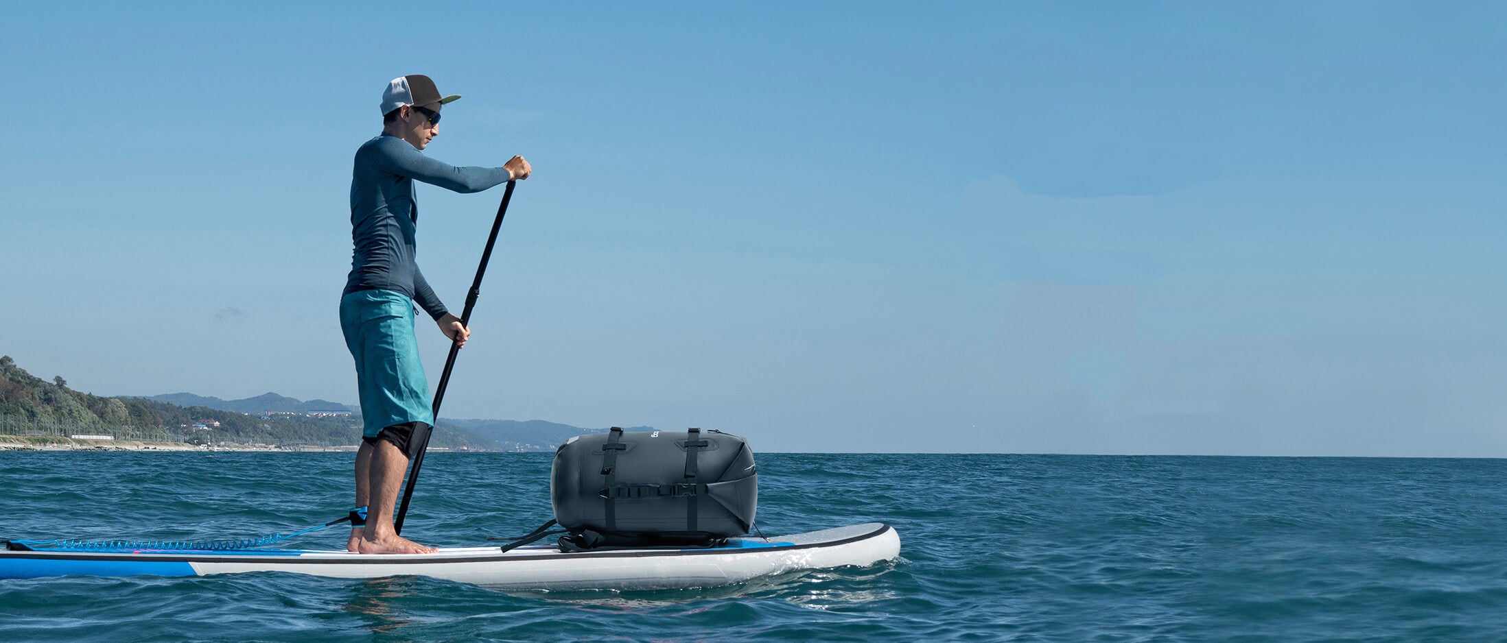 Person paddleboarding on a calm ocean with a clear blue sky and the idrybag waterproof drybag