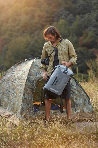 Person standing next to a tent with a gray idrybag waterproof drybag in a forest setting