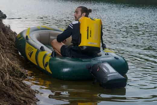 Man sitting in an inflatable boat with a motor on a body of water also with yellow idrybag waterproof pro lite bag